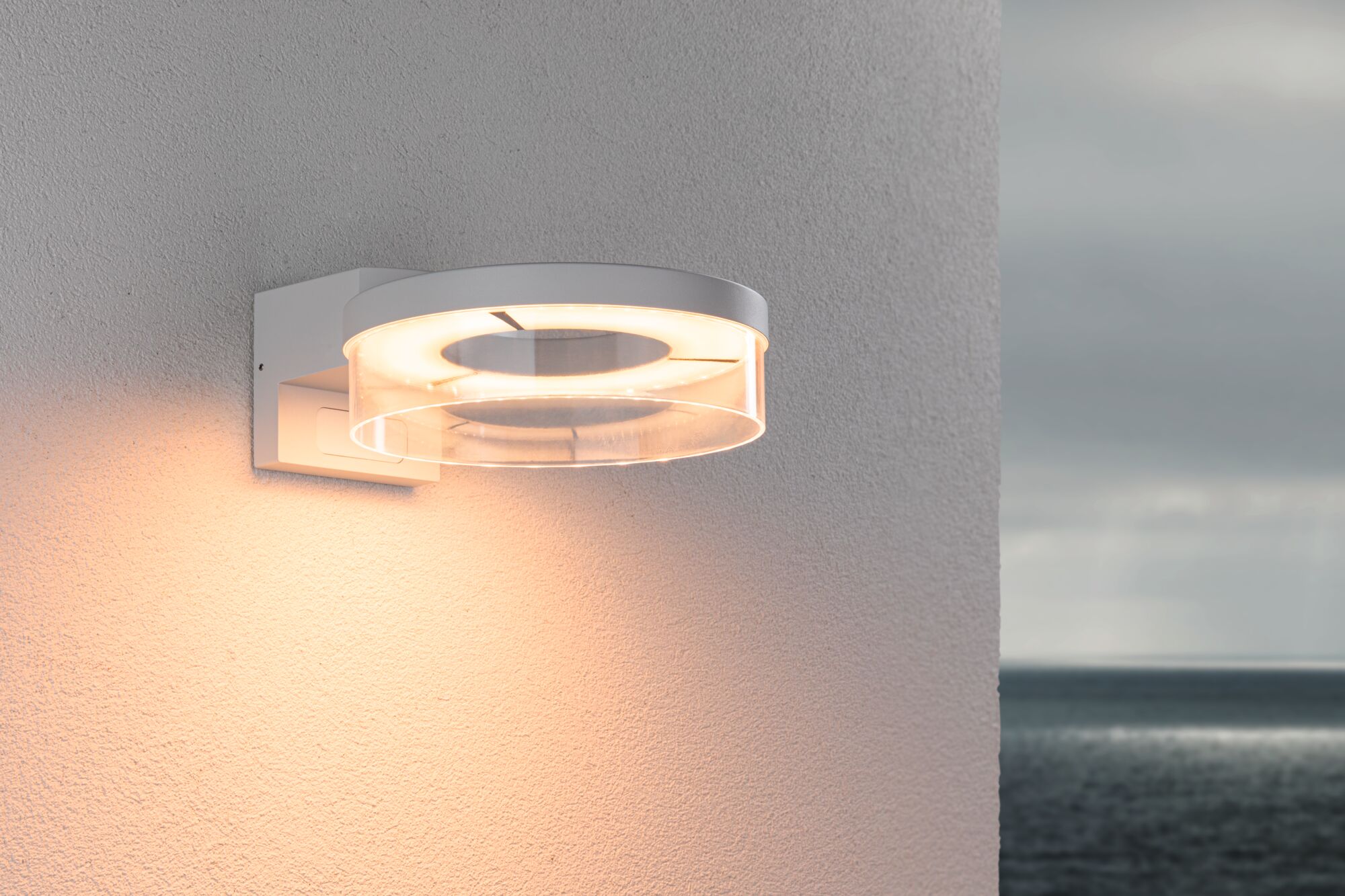 Modern white LED wall light with transparent ring and warm white light for outdoor use.