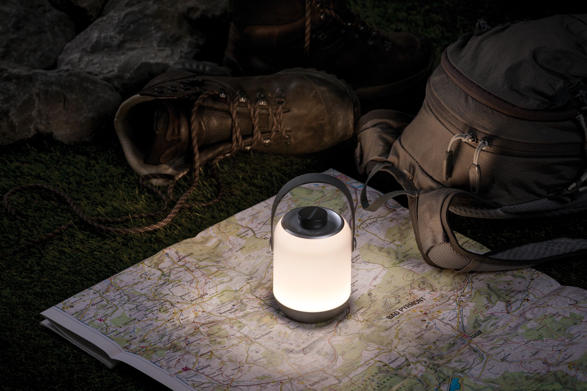 Lanterne LED blanche portable sur carte à côté de bottes de randonnée marron et sac à dos gris pour activités extérieures