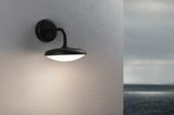 Schwarze Außenwandleuchte mit rundem, weißem Diffusor an grauer Wand mit Meerblick, LED Außenlampe