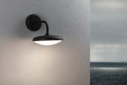 Schwarze Außenwandleuchte mit rundem, weißem Diffusor an grauer Wand mit Meerblick, LED Außenlampe