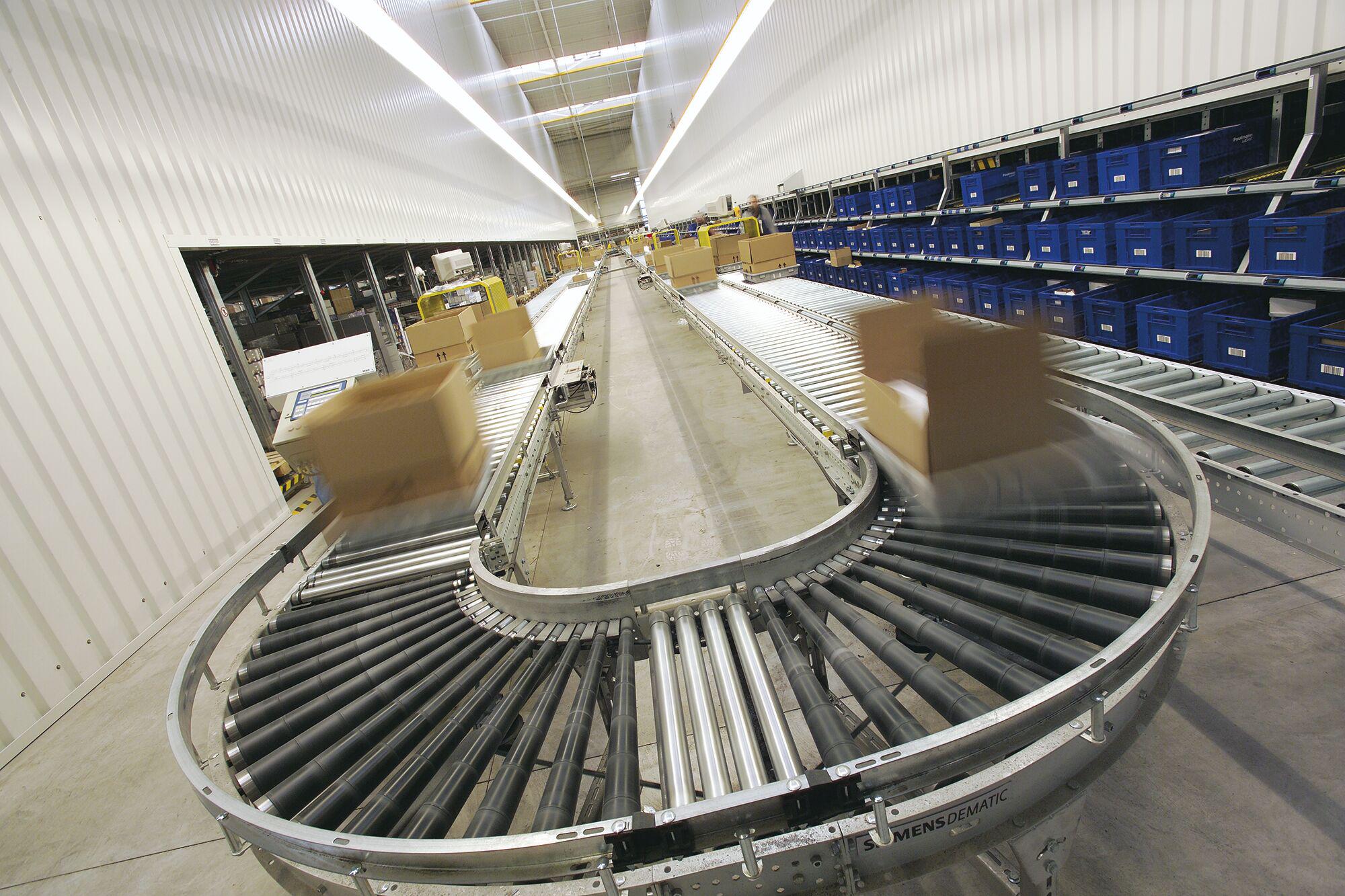 Moderne Förderanlage mit braunen Kartons auf Rollenbahn in Lagerhalle mit blauen Lagerboxen