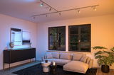 Moderne woonkamer met grijze stoffen bank, zwarte meubels en gekleurde LED-plafondspots voor accentverlichting