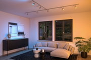 Modernes Wohnzimmer mit grauem Stoffsofa, schwarzen Möbeln und farbigen LED-Deckenstrahlern für Akzentbeleuchtung