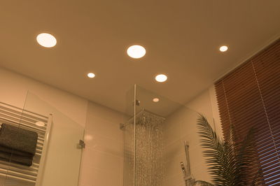 Salle de bain moderne avec spots LED encastrés blanc chaud au plafond et douche pluie en acier inox.