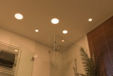 Modernes Badezimmer mit warmweißen LED-Einbaustrahlern in der Decke und Regendusche aus Edelstahl.