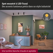 Salon moderne avec mur vert et spots LED noirs au plafond diffusant une lumière blanche chaude