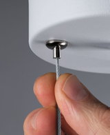 Nærbillede af hånd, der holder stålkabel fastgjort til hvid lampe med metalbeslag, belysningstilbehør.