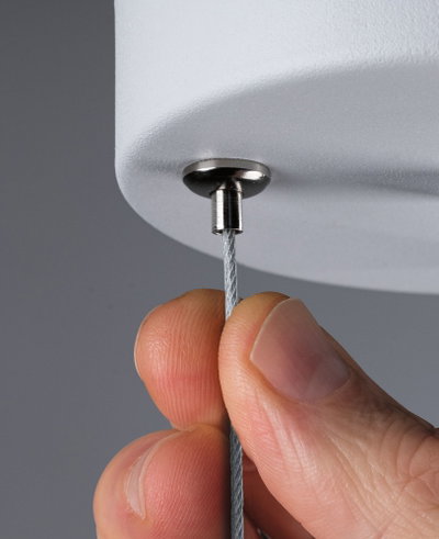 Nærbillede af hånd, der holder stålkabel fastgjort til hvid lampe med metalbeslag, belysningstilbehør.