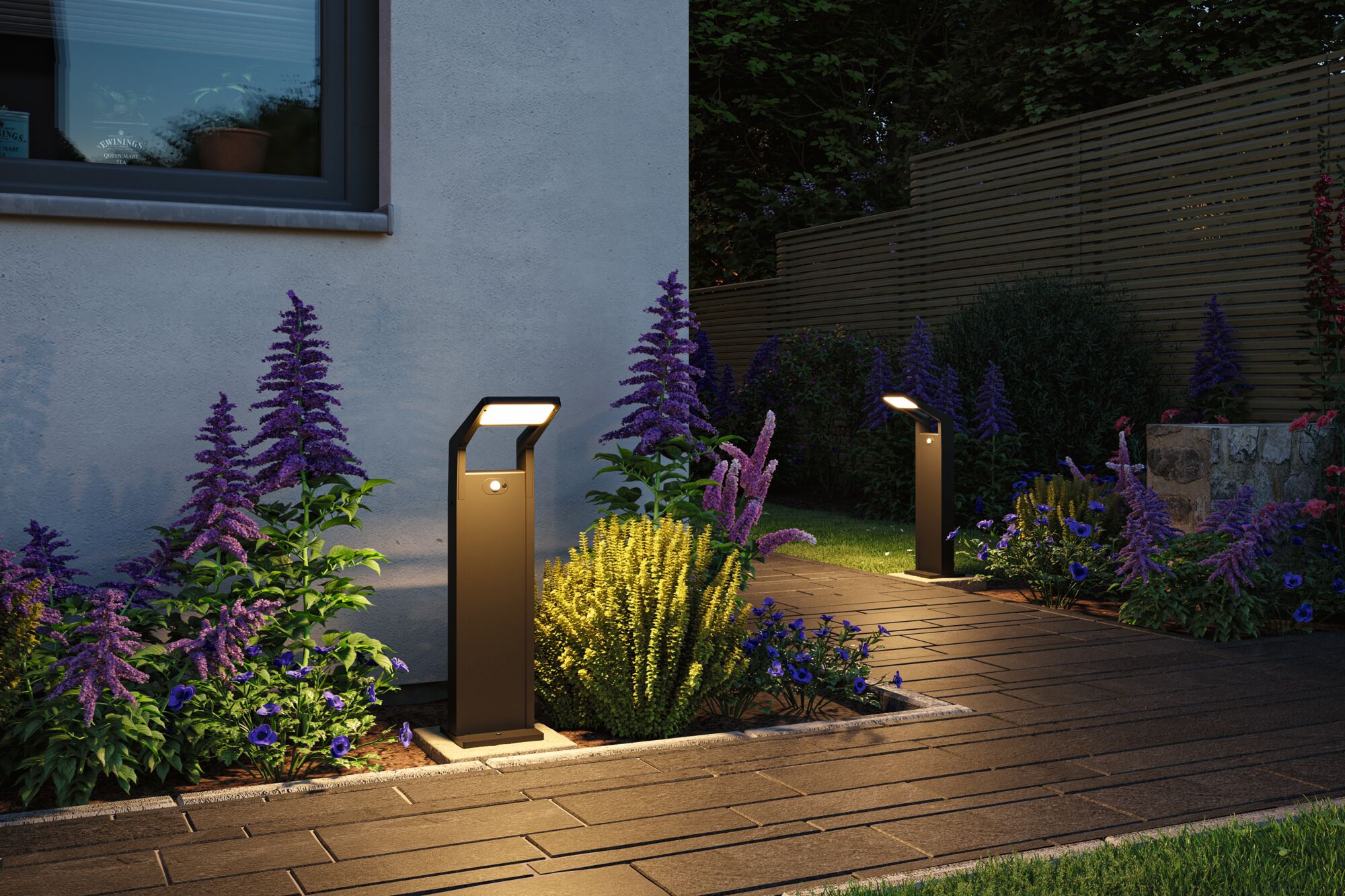 Modern anthracite metal LED path lights illuminating garden path with purple and yellow flowers.