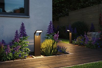 Modern anthracite metal LED path lights illuminating garden path with purple and yellow flowers.