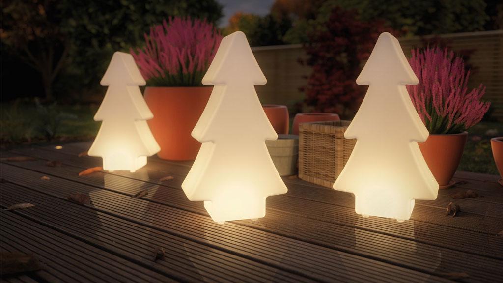 Drie witte LED-decoratieve plastic bomen verlichten een terras met planten op de achtergrond.