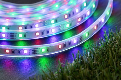 Colorful RGB LED light strips on dark surface near green grass, flexible decorative lighting solution