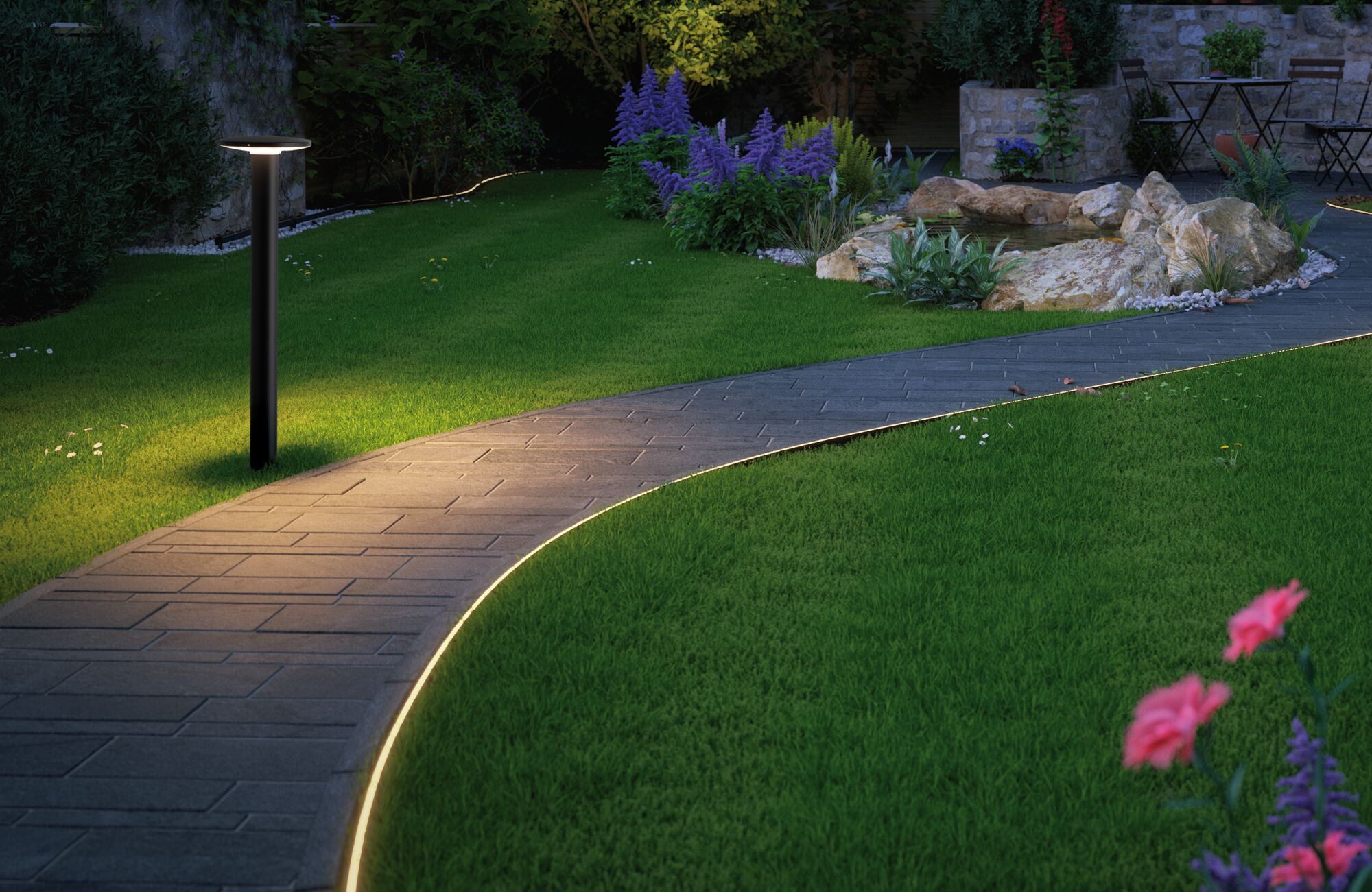Black LED garden light illuminating curved stone path with grass and flowers in outdoor setting.