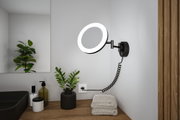 Schwarze LED-Wandleuchte mit rundem Leuchtring und flexiblem Arm über Holzablage im Badezimmer.