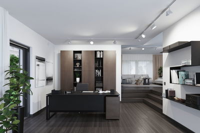 Modern office with black desk, brown wooden shelves and LED ceiling spotlights for task lighting