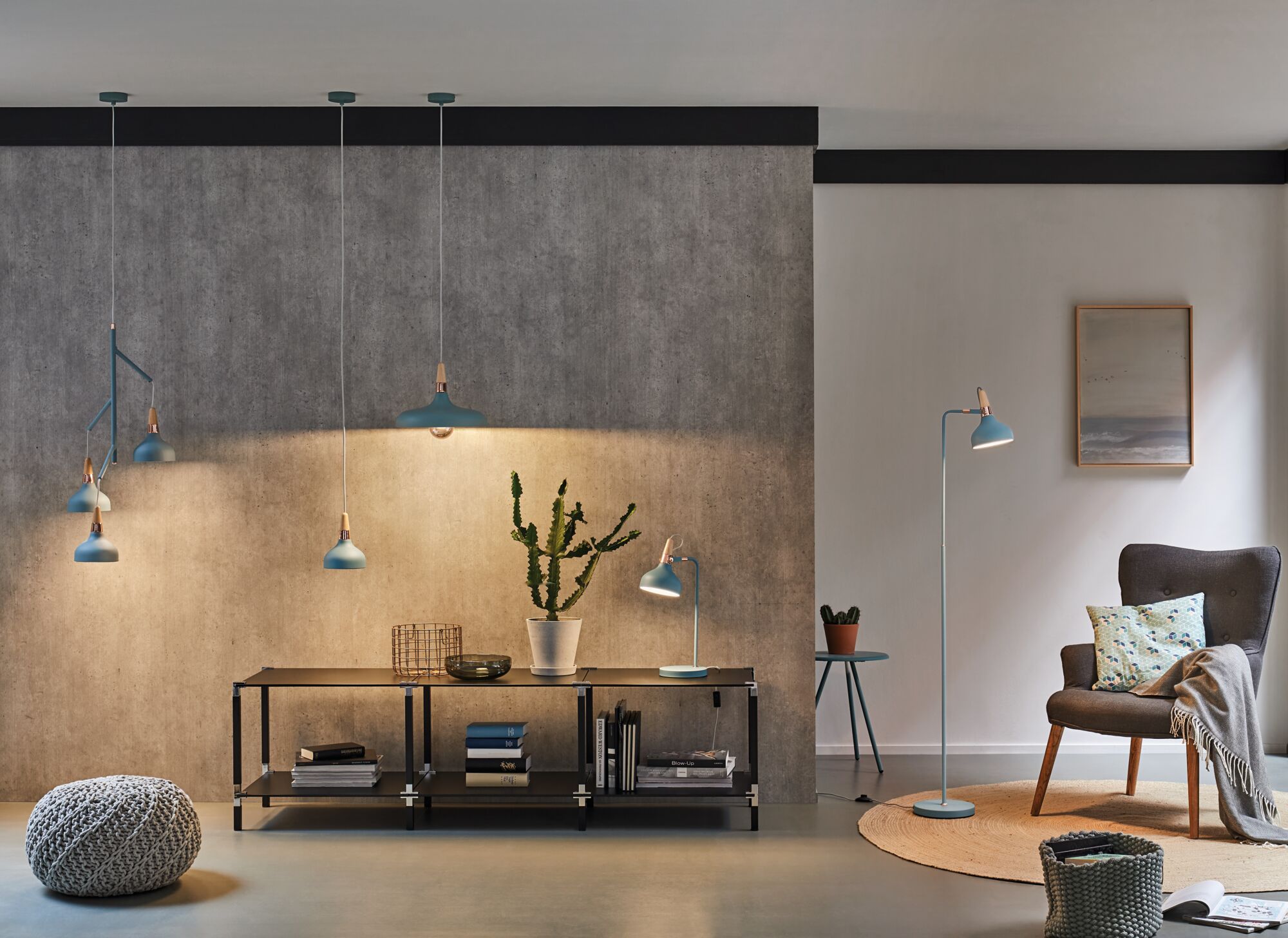 Moderne stue med blå metal lamper, gulvlampe, pendellamper og bordlampe, betonvæg og grå lænestol.