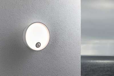 Runde weiße Außenwandleuchte mit Bewegungsmelder an grauer Wand, geeignet für Außenbeleuchtung.