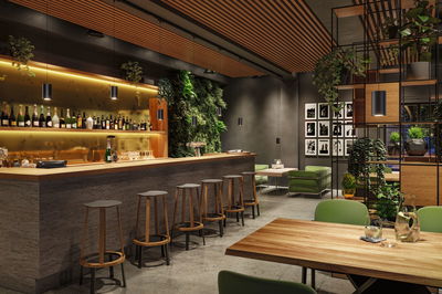 Modern bar interior with wooden counter, green chairs, plants, and black pendant lights for ambient lighting