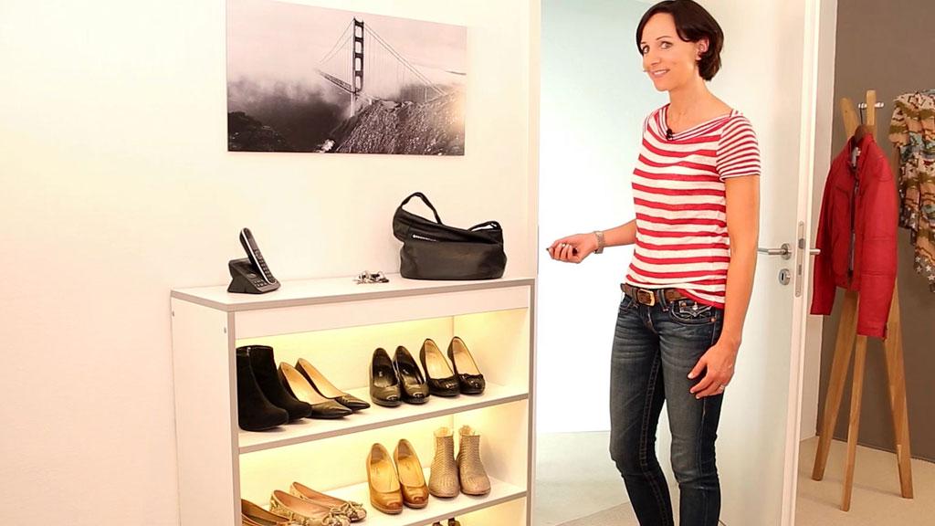 Woman standing by white shoe cabinet with LED lighting and various black and brown women's shoes.