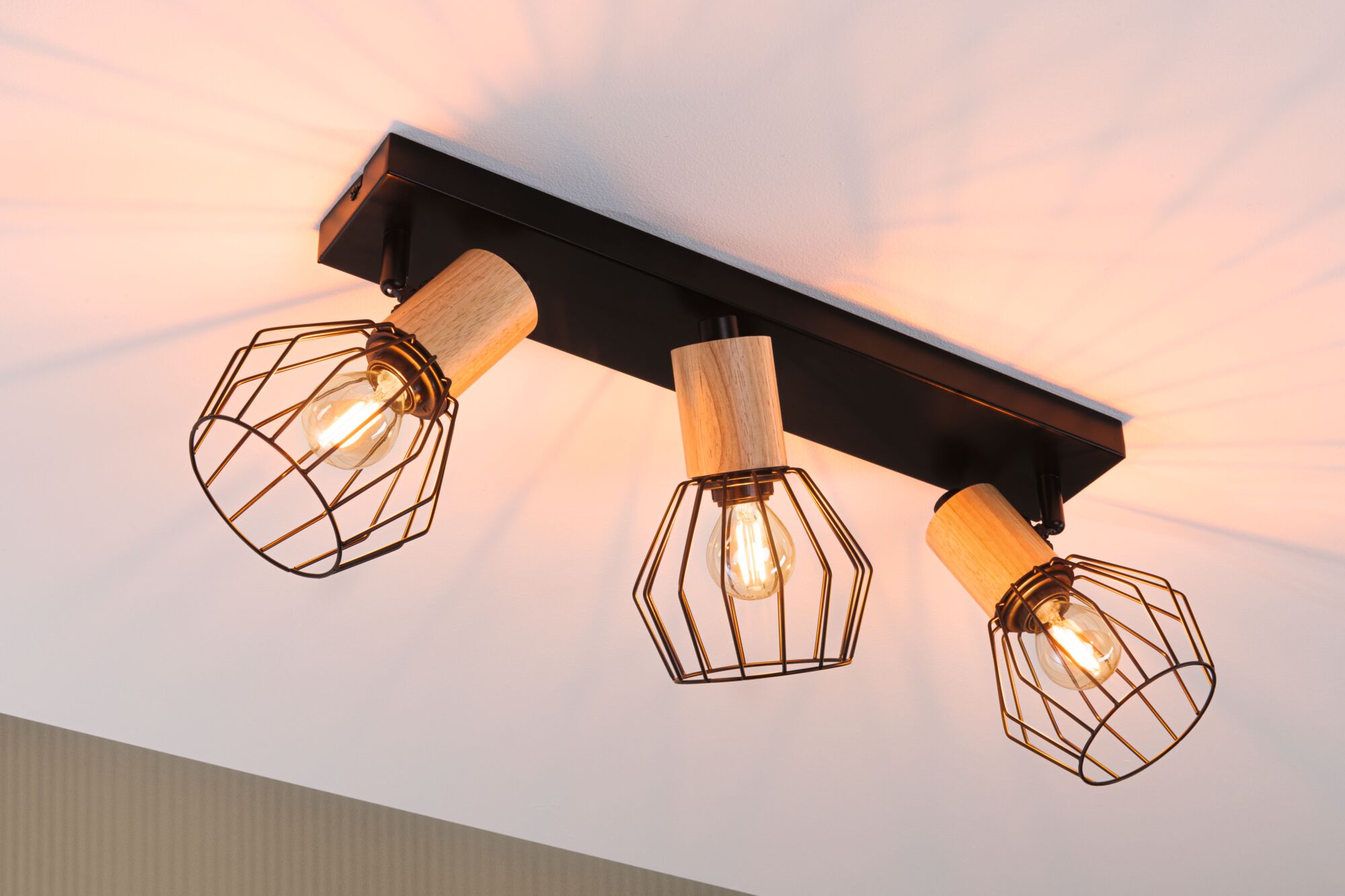 Plafondlamp met drie zwarte metalen kooien en houten accenten, warm licht voor woonruimte