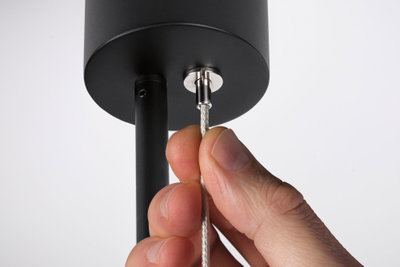 Hand holding silver steel cable on black metal pendant for modern LED hanging light.