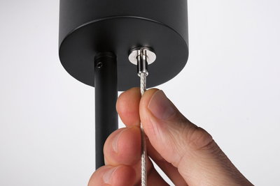 Hand holding silver steel cable on black metal pendant for modern LED hanging light.