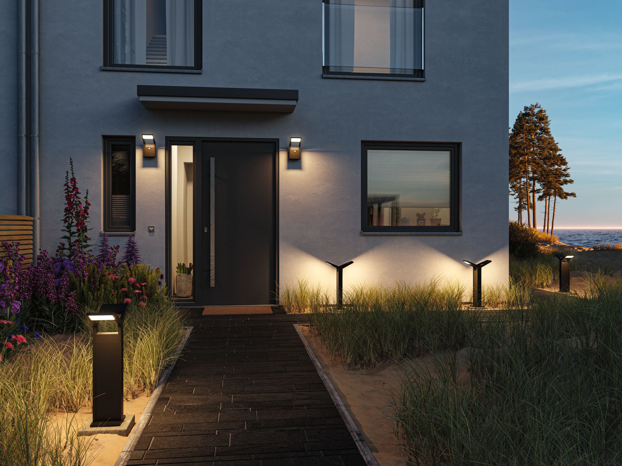 Moderne schwarze Außenleuchten aus Metall beleuchten den Weg und die Fassade eines Hauses am Meer bei Abendlicht.