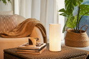 White ceramic table lamp with geometric pattern beside brown sofa and woven basket with plant