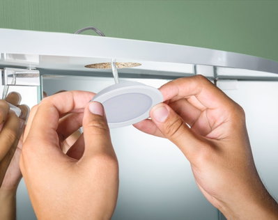 Hænder monterer hvid LED-indbygningslampe i plast i loft med grøn baggrund