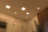 Moderne vierkante LED-plafondlampen in warm wit verlichten een douche met glazen wand en houten jaloezieën.