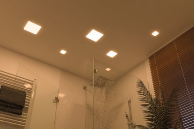 Luminaires LED carrés modernes en blanc chaud éclairent une douche avec paroi en verre et stores en bois.