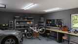 Moderne Garage mit grauem Auto, weißem Fahrrad auf Ständer und LED-Deckenleuchten für Werkstattbeleuchtung