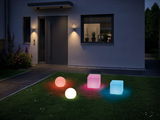 Bunte LED-Gartenleuchten in Kugel- und Würfelform auf Rasen vor modernem Haus bei Nacht.