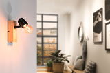 Wall lamp with wooden base and black metal head, warm light in modern living space with window view.