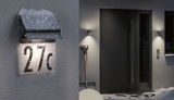 Illuminated house number 27c with black metal roof and snow on exterior wall at night