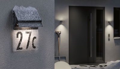 Illuminated house number 27c with black metal roof and snow on exterior wall at night