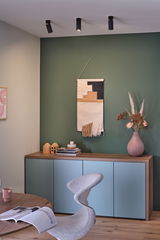 Drei schwarze Deckenstrahler aus Metall in modernem Wohnzimmer mit grünem Wandakzent und Sideboard.