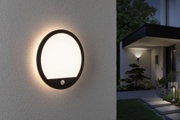Round outdoor wall light with black frame and warm white glow on house exterior at night