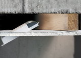 Weißer Kunststoff-Wandanschluss mit grauem Deckel auf Beton und Holz für LED-Beleuchtungssysteme.
