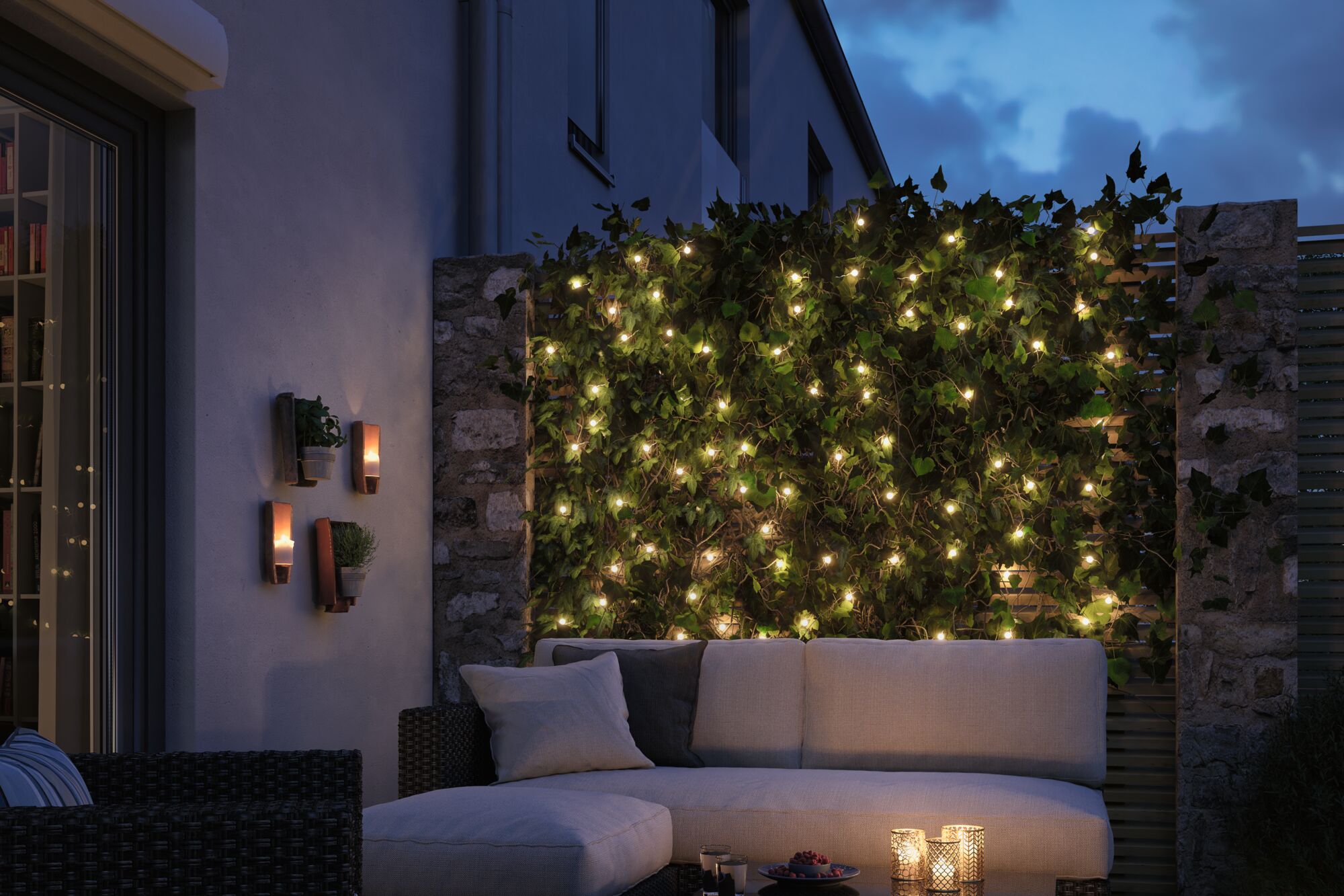Gemütliche Terrasse mit LED-Lichterkette an grünem Efeu und beigem Polstersofa bei Abenddämmerung
