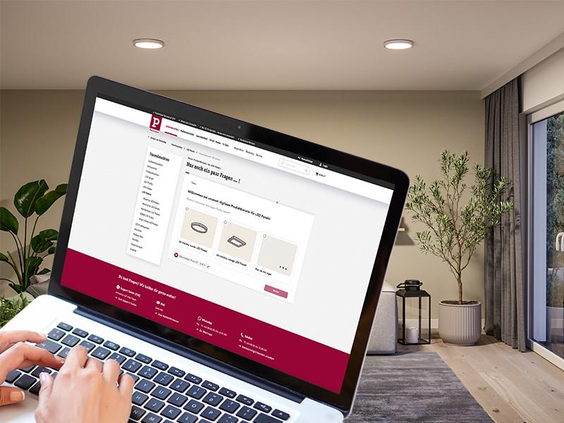 Laptop zeigt LED-Panel Auswahl auf Paulmann Webseite in modernem Wohnzimmer mit Deckenleuchten.