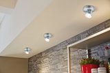 Three silver LED ceiling spotlights on beige ceiling with gray stone wall and red flower pot.