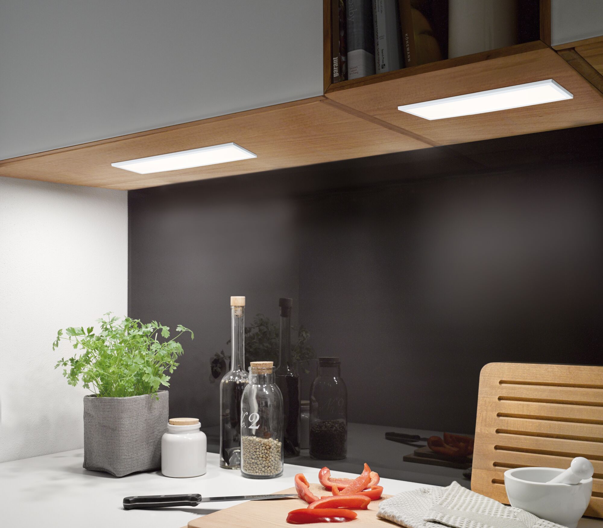 Modern LED under-cabinet lights in wooden kitchen shelf with herb pot and cutting board with sliced pepper