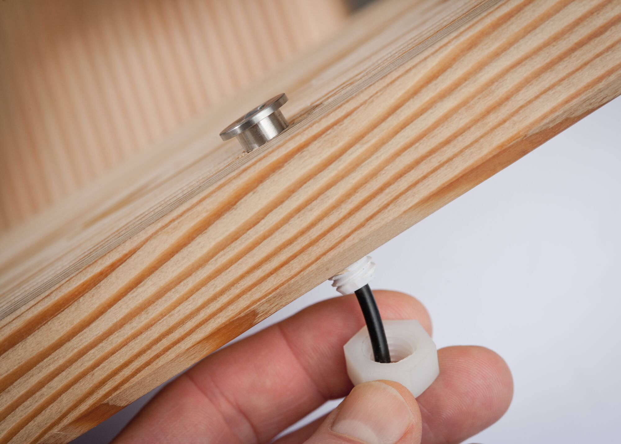 Hand bevestigt zwarte kabeldoorvoer met wit kunststof op licht houten paneel voor LED-verlichting