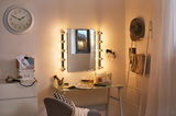Lighted vanity mirror with bulbs on glass table in cozy room featuring clock and decor items.