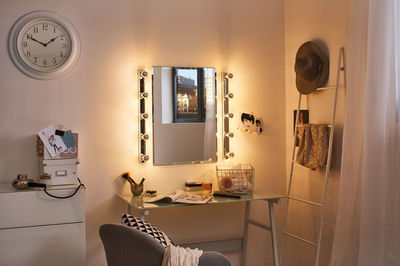 Verlicht make-upspiegel met lampen op glazen tafel in gezellige kamer met klok en decoratie.