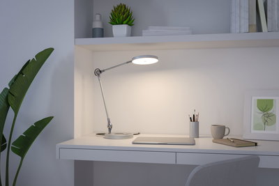 Moderne hvid metal skrivebordslampe med rund lyskilde på minimalistisk arbejdsplads.