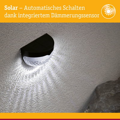Schwarze Solar-Wandleuchte mit integriertem Dämmerungssensor leuchtet weiß an strukturierter Wand