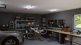 Modern garage with grey car, white bike on stand, workbench with tool board and LED ceiling lights
