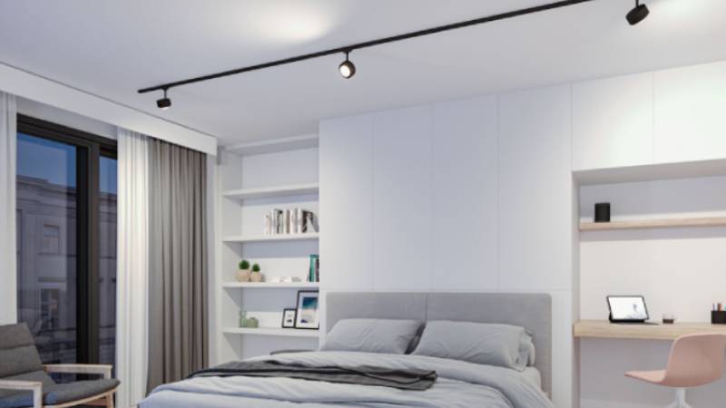 Chambre moderne avec éclairage sur rail URail noir au-dessus d'un lit gris et d'une armoire blanche